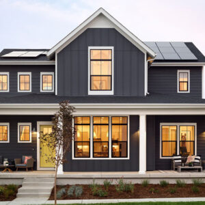 Double-hung and picture windows on a dark grey home with white trim and yellow front entry door