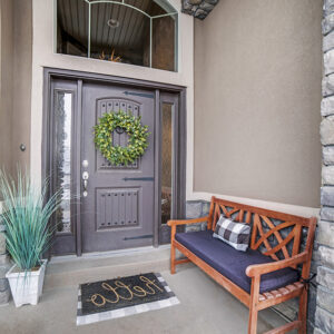 Large entryway at a residential property with a steel front entry door, wooden bench, rug, and plant.